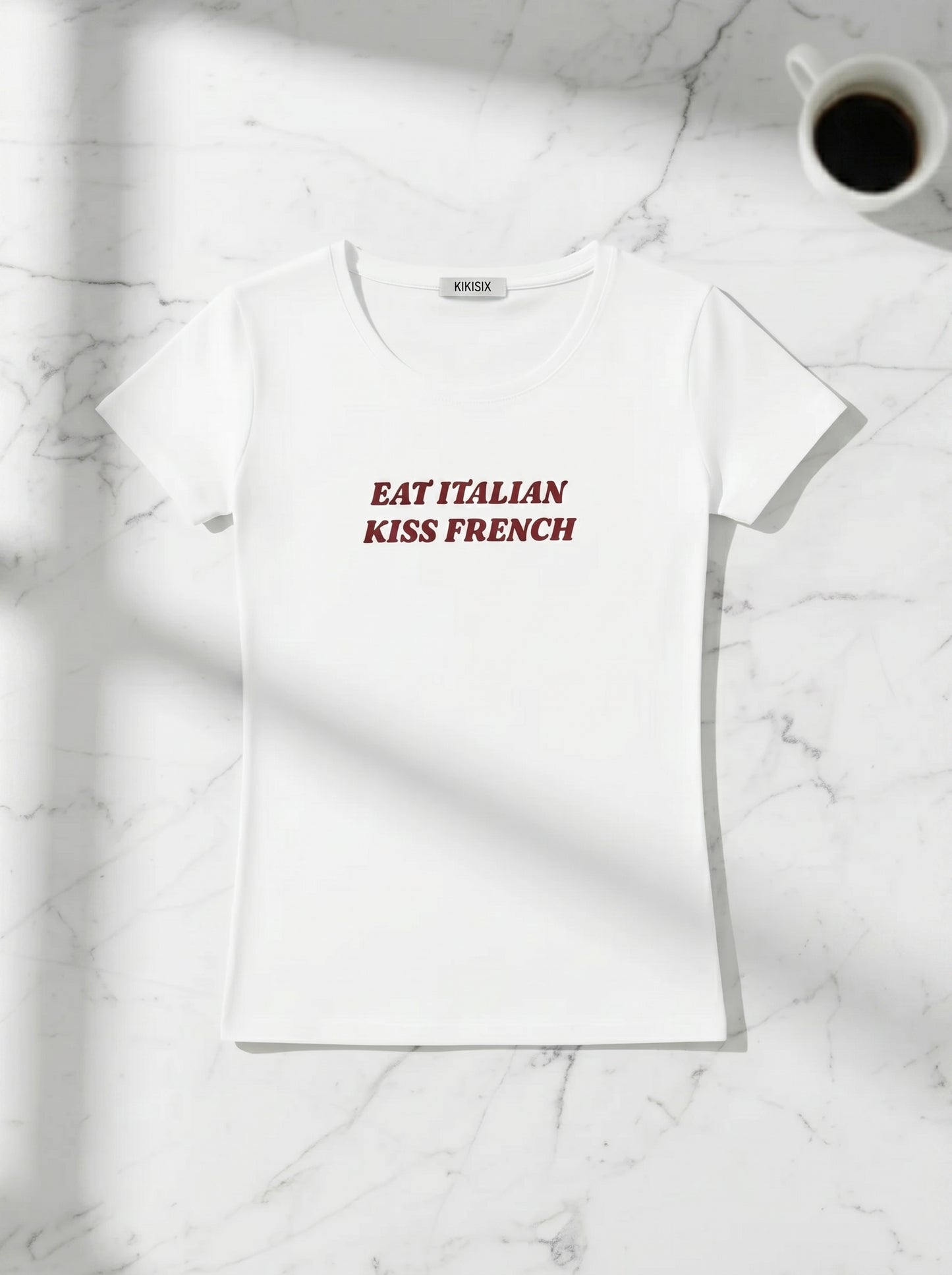 Balti marškinėliai „Eat Italian Kiss French“ Kikisix ant stalo