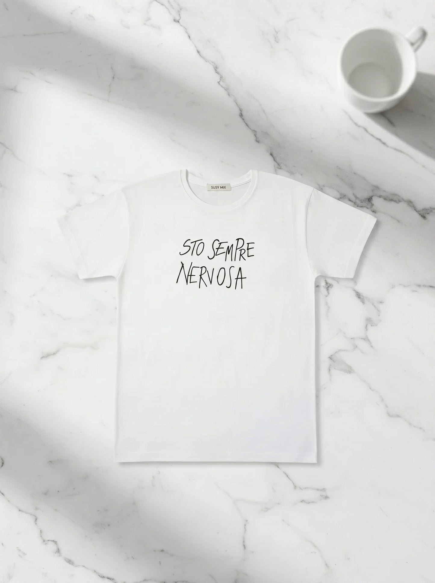 Balti marškinėliai „Sempre Nervosa“ Susy Mix ant stalo