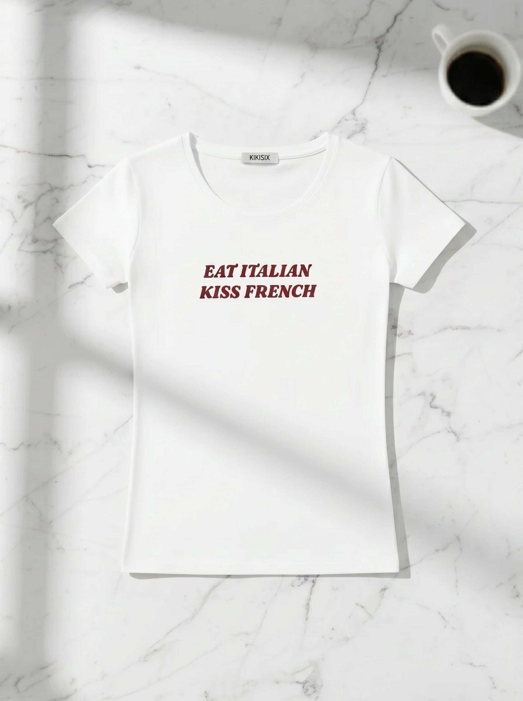 Balti marškinėliai „Eat Italian Kiss French“ Kikisix ant stalo